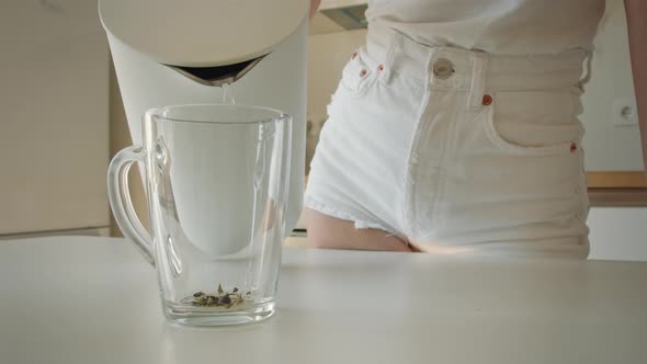 A Young Woman is Pouring Water Into a Cup From a Teapot