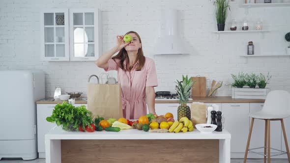 Pretty woman standing in kitchen. Young woman playing with fruits in the kitchen