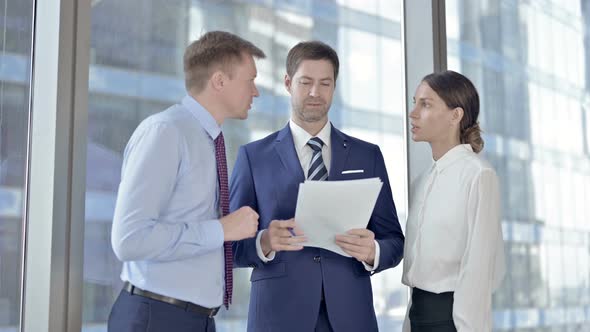 Middle Aged Businessman Having Reading and Discussion on Documents with His Assistants