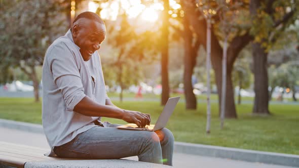 Cheerful Carefree Senior Black Man Sitting Outdoor Using Laptop Plays Having Fun Laughing Pretending