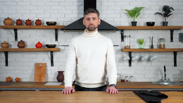 Portrait serious chef man in white sweater looking camera at home kitchen