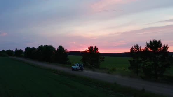 Aerial View of a Car Driving in Nature on a Field at Sunset