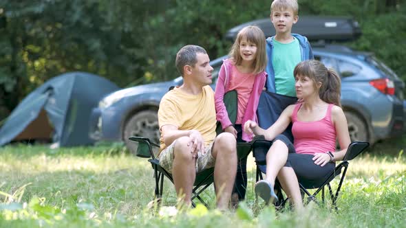 Happy young family enjoying time at capmsite outdoors. Parents and their children chatting 