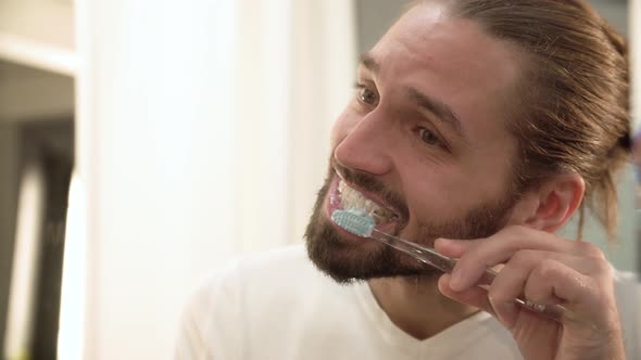 Man Brushing Teeth And Looking At Mirror In Bathroom