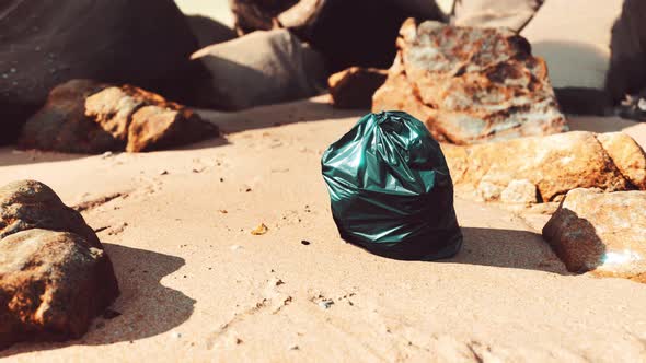 Black Plastic Garbage Bag Full of Trash on the Beach