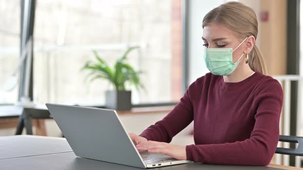 Young Woman with Face Mask Using Laptop in Office 