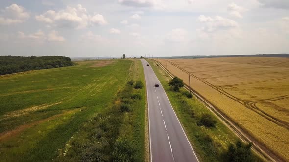 Aerial view of a road with moving cars between yellow agriculture wheat fields ready