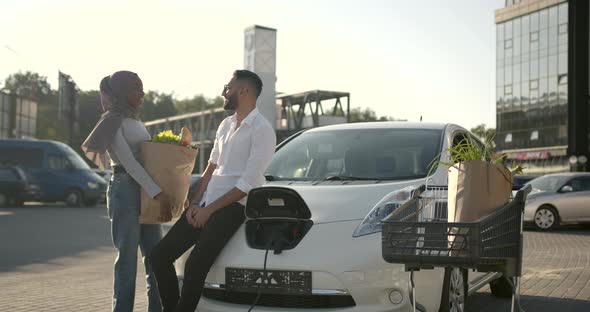 Couple Talking While Charging Electric Car at Station