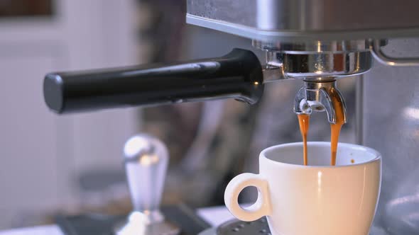 Fresh Coffee Pouring Down From Portafilter of Espresso Machine Into White Ceramic Cup