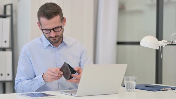 Middle Aged Man Checking Empty Wallet While Working on Laptop