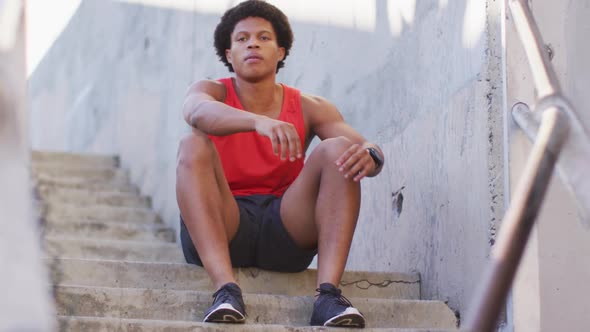 African american man exercising in city, sitting on steps and tying shoelaces