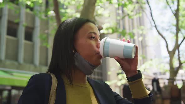 African american woman wearing face mask drinking coffee in city park