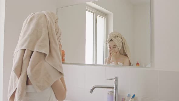 Teenage girl applying moisturizer to her face in front of the bathroom mirror