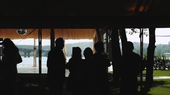 Silhouettes of People Talking Standing in Restaurant with Panoramic View to the River Slow Motion