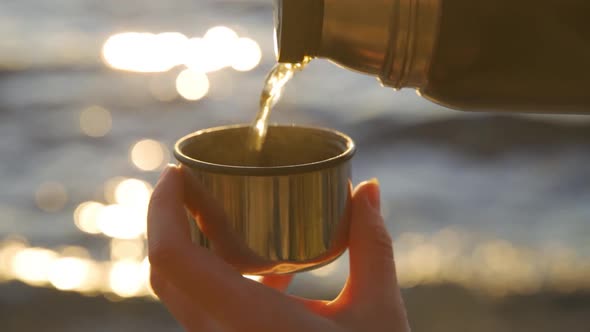 Warming Tea with Lemon and Ginger is Poured From a Thermos Against the Backdrop of the Lake