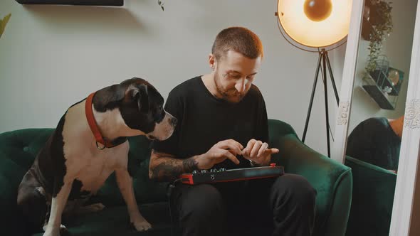 Young Bearded European Man Creating Music on MIDI Controller Keyboard While Black and White Amstaff