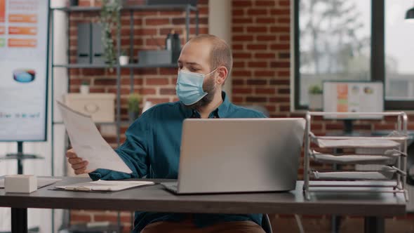 Portrait of Employee Analyzing Charts Papers and Using Laptop