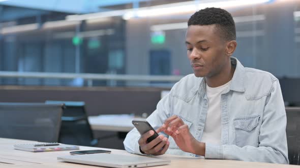 African Man Celebrating Success on Smartphone in Office