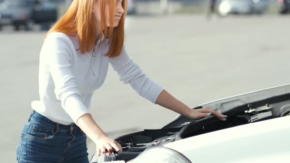 Young stressed woman driver near broken car with popped hood having a prbreakdown 