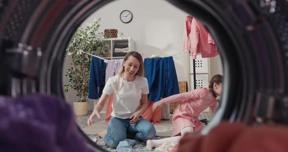 Mother and Daughter are Sitting on the Laundry Room Floor Playing Together Tossing Clothes Up