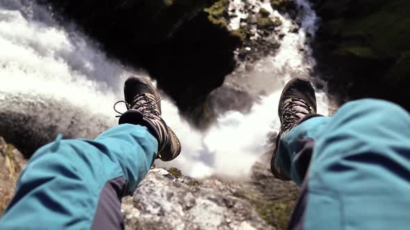 Person sitting above a beautiful waterfall, slow motion shot at day time of hiker in Norway, Europe.