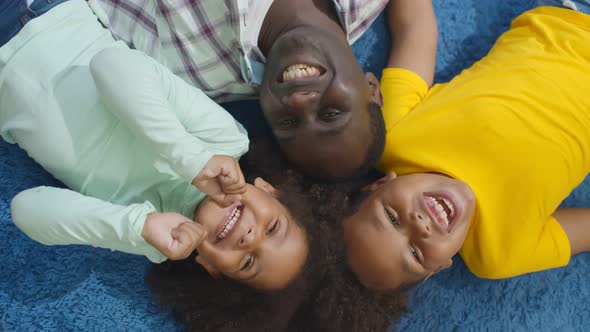 Top View of Smiling African Father with Little Son and Daughter Lying on Blue Carpet and Looking at