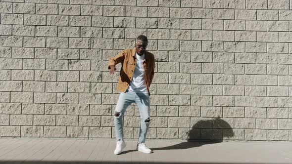 Joyful AfroAmerican Dancer Having Fun Moving Legs and Dancing Outside Against Brick Wall