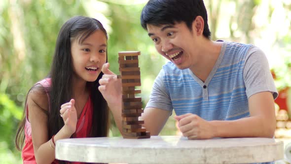 Asian girl playing a game of risk trying to move wooden blocks with father.