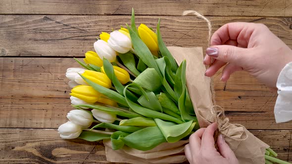 Hands untie a tulips bouquet on a wooden table top view 
