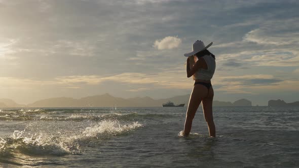 Woman In Thong And Sun Hat Walking In Sea