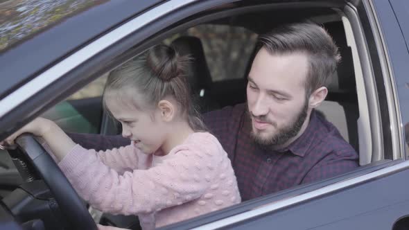 Portrait Little Girl Sitting on Father's Lap in the Car Close Up. The Child Is Learning To Drive