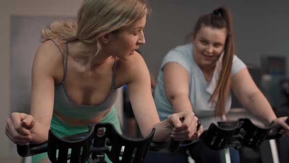 Two caucasian women ride a bikes at the gym. Shot with RED helium camera in 4K.