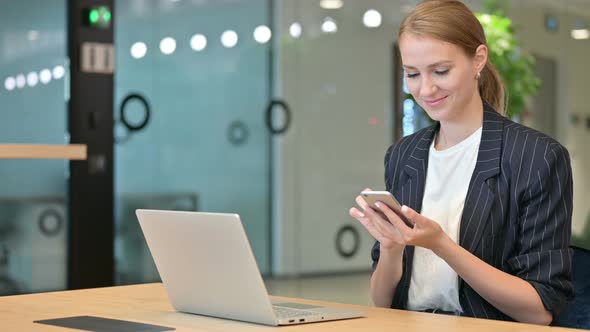 Professional Businesswoman with Laptop Using Smartphone in Office 