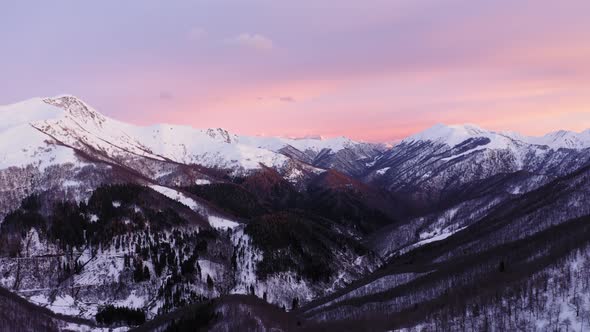 Aerial View of Snow Covered Mountain Range During Pink and Yellow Sunset or Sunrise, Dark Forest 