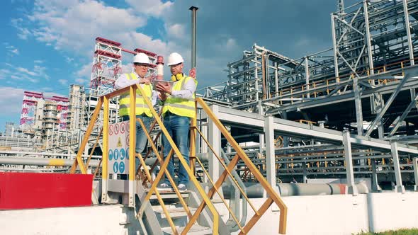 Outside Premises of the Oil Refinery with Two Workers Talking