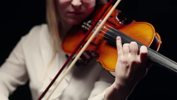 Woman Violinist Plays the Violin with a Bow and Fingers on the Strings in Studio a Dark Background