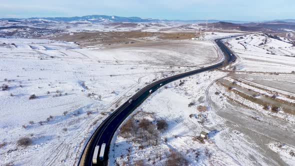 Aerial View of a Winding Asphalt Road with Driving Cars in a Frosty Winter Day