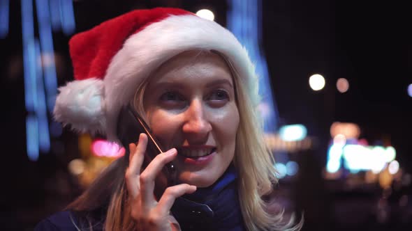 a woman chatting on her smartphone wearing a Santa hat is a night city.