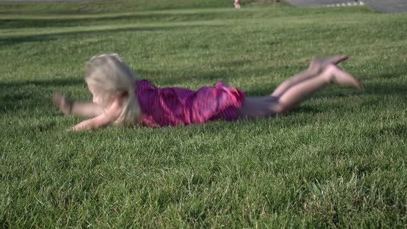 Happy Baby Girl Slides Down the Grass From a Green Hill in the Park