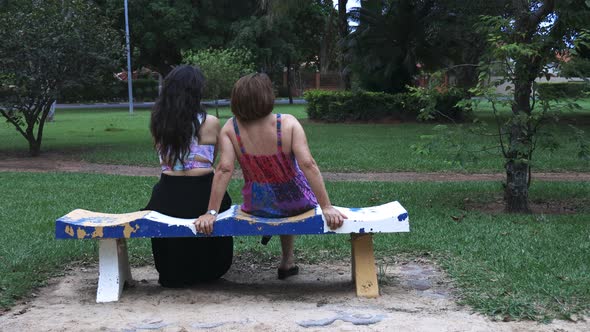 Mother and daughter sitting on a bench in the park talking to each other and chilling down