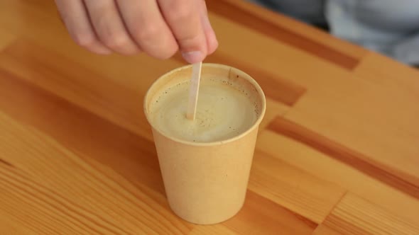 Close-up of male hand with stick interferes with craft cup with coffee on wooden table