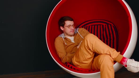 Young Man with Mobile Phone Sitting in Ball Chair on Black Background