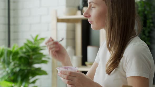 Young Woman Eating Yogurt in the Kitchen at Home