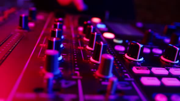 Closeup of Dashboard Mixing Console Illuminated By Neon Buttons of Which are Pressed By DJ Hand