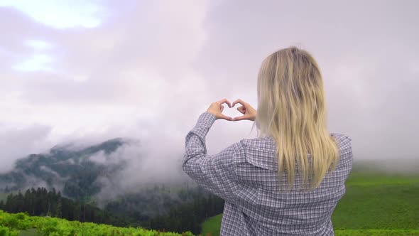 Young girl makes her fingers and hands heart in mountains.