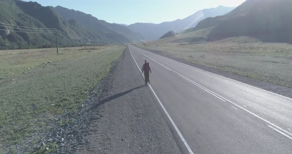 Flight Over Hitchhiker Tourist Walking on Asphalt Road. Huge Rural Valley at Summer Day