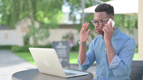 Angry African Man Talking on Smartphone in Outdoor Cafe