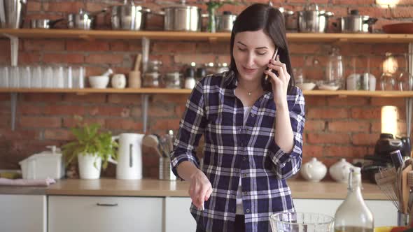 Woman Talking on the Phone and Cooking in the Kitchen Cuts a Cucumber