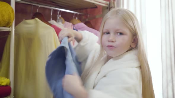 Side Back View of Little Blond Caucasian Girl Taking Out Clothes From Wardrobe and Throwing It Back