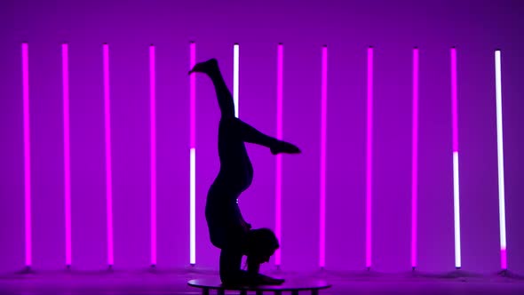 The Athlete Performs Gymnastics Against the Backdrop of Neon Lights